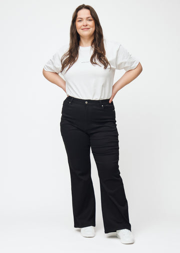 Ganzkörperbild eines Plus-Size-Models in schwarzen hochtaillierten Bootcut jeans.