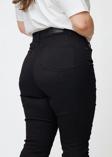 Das Bild zeigt eine Nahaufnahme von schwarzen Plus-Size-High-Rise-jeans für Damen in der Farbe Ravens in skinny Fit von hinten.