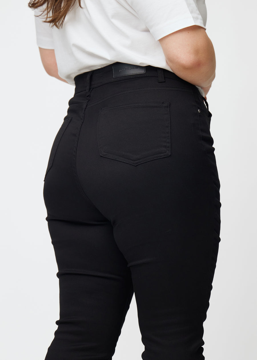 Das Bild zeigt eine Nahaufnahme von schwarzen Plus-Size-High-Rise-jeans für Damen in der Farbe Ravens in skinny Fit von hinten.