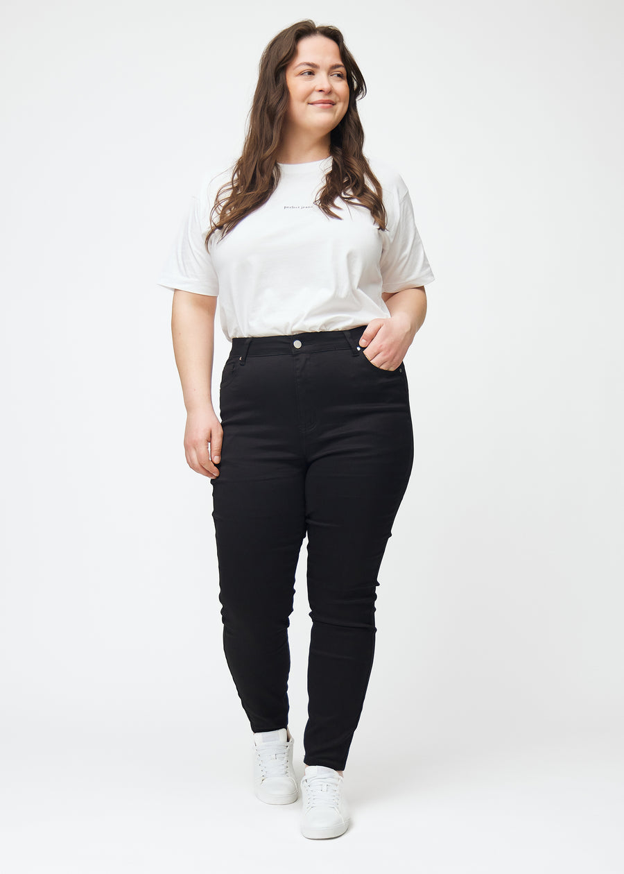 Dies ist eine Ganzaufnahme eines Plus-Size-Models in schwarzen High-Rise-skinny jeans für Damen in der Farbe Ravens.