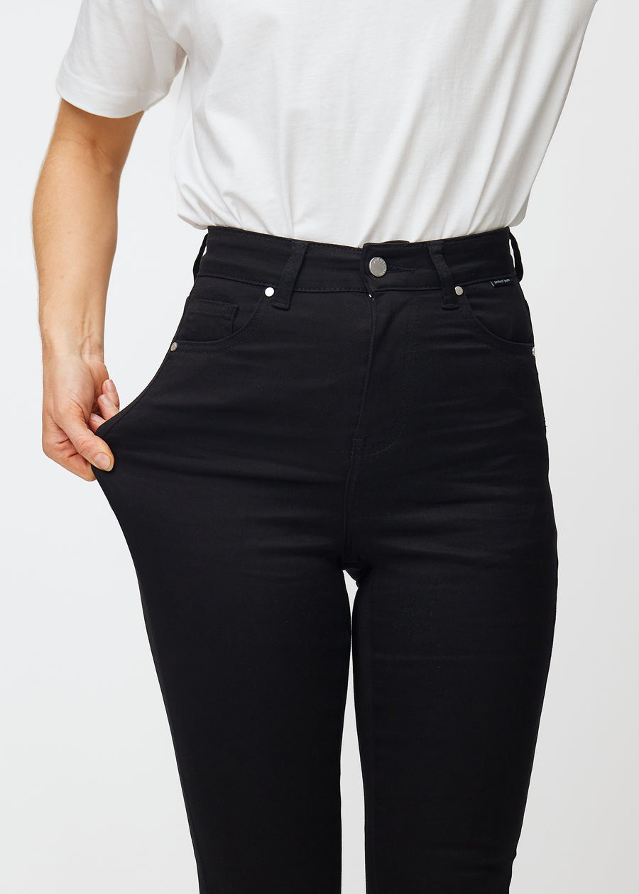 Ein Model dehnt die schwarzen Ravens Stretch-jeans mit hohem Bund, um die Passform zu veranschaulichen.