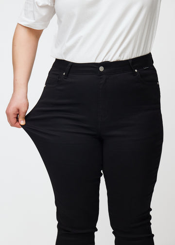 Ein Plus-Size-Model dehnt die schwarzen Stretch-jeans mit hohem Bund in der Farbe Ravens.