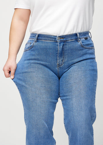 Loose-Jeans für Damen in Blau, Farbe Rivers. Ein Plus-Size-Model dehnt den Jeansstoff am Oberschenkel, um den Stretch zu zeigen.