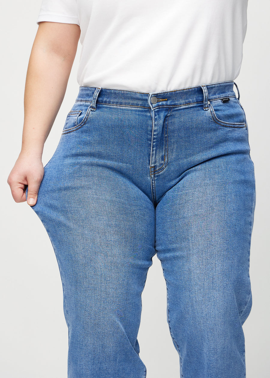 Loose-Jeans für Damen in Blau, Farbe Rivers. Ein Plus-Size-Model dehnt den Jeansstoff am Oberschenkel, um den Stretch zu zeigen.