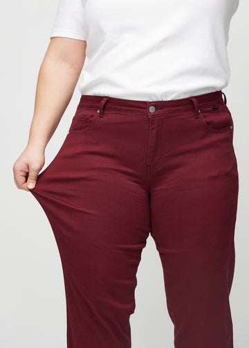 Regular-Jeans für Damen in Dunkelrot, Farbe Santas. Ein Plus-Size-Model dehnt den Stoff am Oberschenkel, um den Stretch zu zeigen.