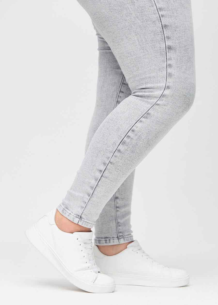Skinny-Jeans für Damen in Hellgrau, Farbe Ashes. Nahaufnahme der eng anliegenden Beinabschlüsse am Knöchel eines Plus-Size-Models.