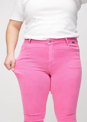 Skinny-Jeans für Damen in Hellrosa, Farbe Flamingos. Ein Plus-Size-Model dehnt den Jeansstoff am Oberschenkel, um den Stretch zu zeigen.
