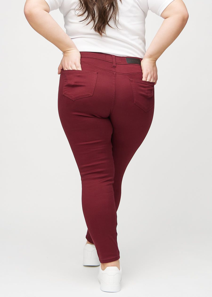 Dunkelrote skinny jeans von hinten an einem Plus-Size-Model gesehen, sodass man das gesamte Produkt sehen kann. 