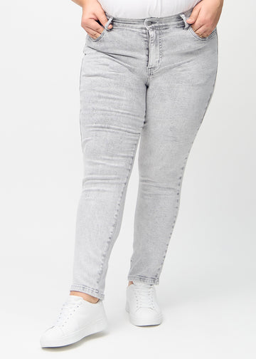 Hellgrauer Denim slim jeans, Modellname Ashes, der eng am Bein anliegt, jedoch am Knöchel etwas lockerer sitzt, an einem Plus-Size-Model, von vorne gesehen.