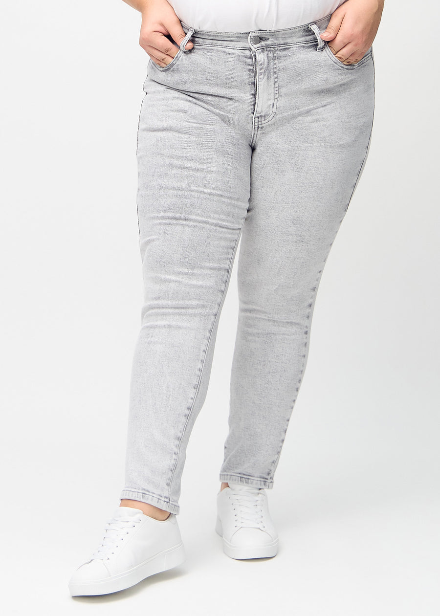 Hellgrauer Denim slim jeans, Modellname Ashes, der eng am Bein anliegt, jedoch am Knöchel etwas lockerer sitzt, an einem Plus-Size-Model, von vorne gesehen.