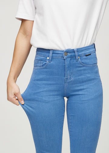 Slim-Jeans für Damen in Blau, Farbe Geraniums. Ein Model zieht am Jeansstoff am Oberschenkel, um den Stretch zu zeigen.