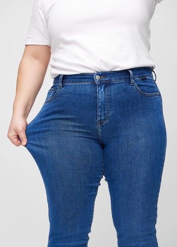 Slim-Jeans für Damen in Dunkelblau, Farbe Oceans. Ein Plus-Size-Model zieht am Jeansstoff am Oberschenkel, um den Stretch zu zeigen.