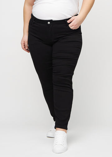 Schwarze slim jeans, Modellname Ravens, die eng am Bein anliegen, jedoch am Knöchel etwas lockerer sind, an einem Plus-Size-Model, von vorn gesehen.
