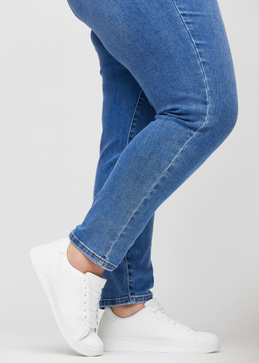 Slim-Jeans für Damen in Blau, Farbe Rivers. Nahaufnahme an den Knöcheln eines Plus-Size-Models, um die Passform am Beinabschluss zu zeigen.