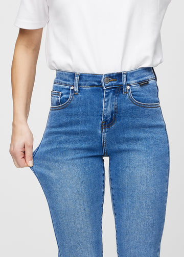 Slim-Jeans für Damen in Blau, Farbe Rivers. Ein Model zieht am Jeansstoff am Oberschenkel, um den Stretch zu zeigen.