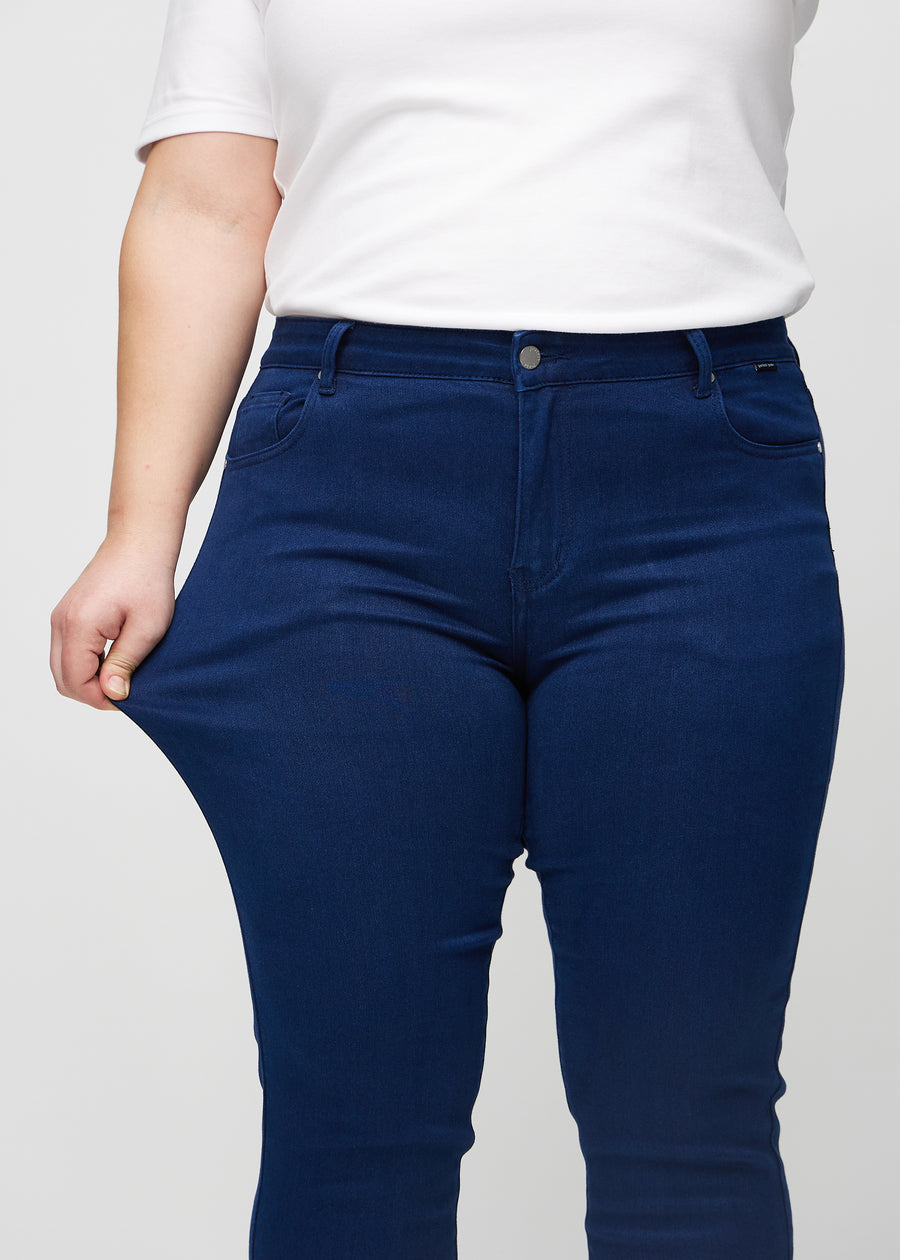 Slim-Jeans für Damen in Dunkelblau, Farbe Royals. Ein Plus-Size-Model zieht am Jeansstoff am Oberschenkel, um den Stretch zu zeigen.