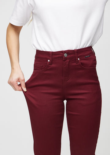 Slim-Jeans für Damen in Dunkelrot, Farbe Santas. Ein Model zieht am Jeansstoff am Oberschenkel, um den Stretch zu zeigen.