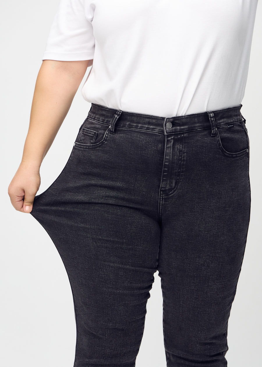 Slim-Jeans für Damen in Dunkelgrau, Farbe Shadows. Ein Plus-Size-Model zieht am Jeansstoff am Oberschenkel, um den Stretch zu zeigen.