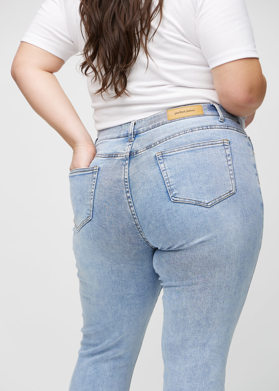 Heller Denim slim jeans von hinten in Nahaufnahme an einem Plus-Size-Model, um Details zu zeigen.