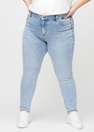 Heller Denim slim jeans, Modellname Waves, die eng am Bein anliegt, jedoch an den Knöcheln etwas lockerer sitzt, an einem Plus-Size-Model, von vorn gesehen.
