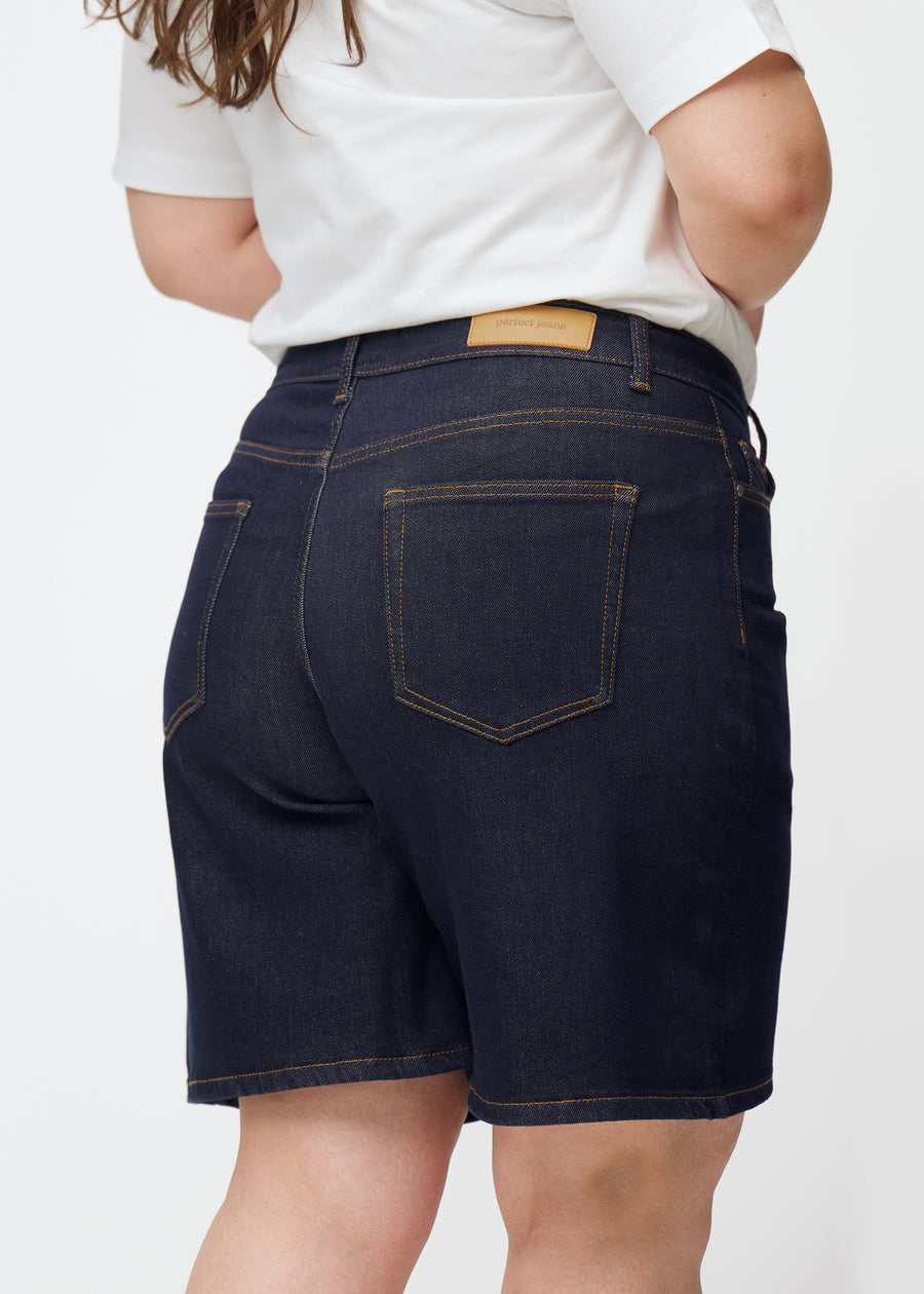 Tief dunkelblaue Denim-Shorts für Damen in der Farbe Midnights von hinten nah auf einem Plus-Size-Model aufgenommen.