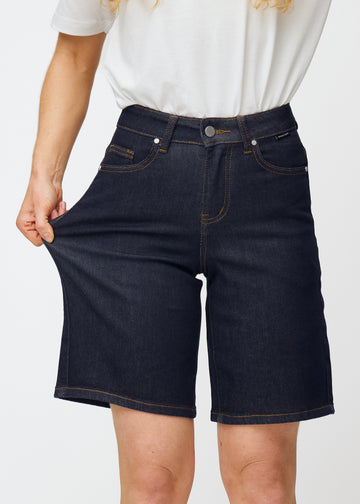 Model dehnt tief dunkelblaue Denim-Shorts für Damen in der Farbe Midnights am Oberschenkel, um den Stretch des Materials zu zeigen.