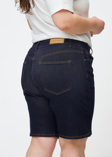 Tief dunkelblaue Denim-Shorts für Damen in der Farbe Midnights von hinten nah auf einem Plus-Size-Model aufgenommen.