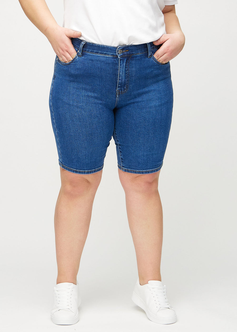 Dunkle Denim-skinny middle shorts, Modellname Oceans, die eng am Oberschenkel anliegen und knapp über dem Knie enden, an einem Plus-Size-Model von vorne gesehen.