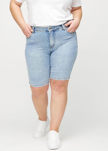 Helle Denim-skinny Middle Shorts, Modellname Waves, die eng am Oberschenkel anliegen und knapp über dem Knie enden, an einem Plus-Size-Model von vorn gesehen.