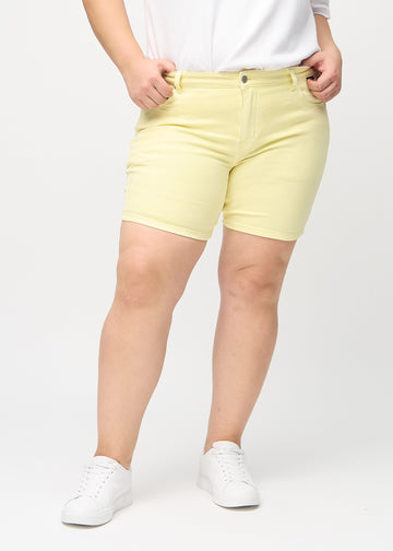 Hellgelbe skinny Short Shorts, Modellname Lemonades, die eng anliegen und bei einem Plus-Size-Model bis zur Mitte des Oberschenkels reichen, von vorne gesehen.