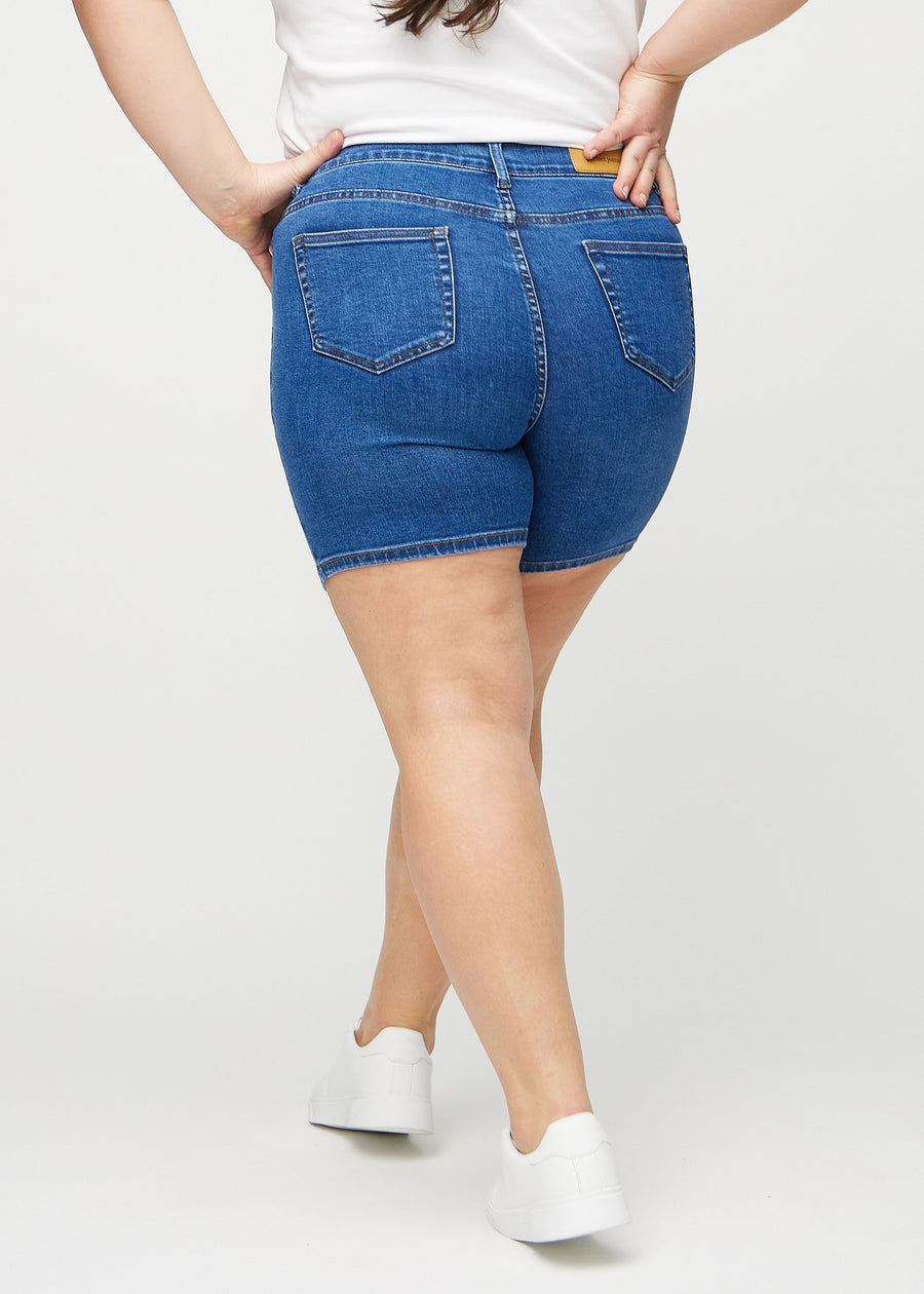 Dunkle Denim-skinny Short Shorts von hinten an einem Plus-Size-Model gesehen, sodass das gesamte Produkt sichtbar ist.