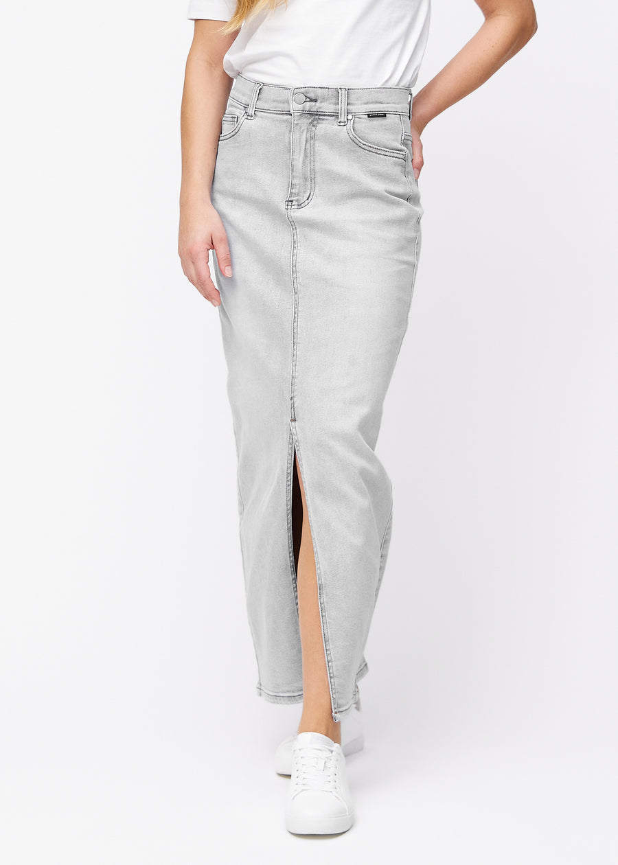 Langer hellgrauer Denimrock für Damen in der Farbe Ashes. Vorderansicht an einem Model, der Rock fällt von der Hüfte gerade bis zum Knöchel und hat vorne einen Schlitz unterhalb des Knies.