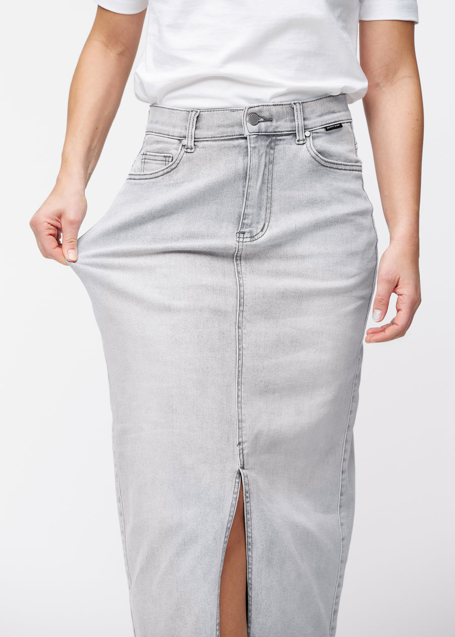 Langer hellgrauer Denimrock für Damen in der Farbe Ashes. Ein Model dehnt den Stoff an der Hüfte, um den Stretch zu zeigen.