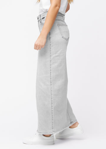 Langer hellgrauer Denimrock für Damen in der Farbe Ashes. Seitenansicht an einem Model mit sichtbarem Schlitz vorne.