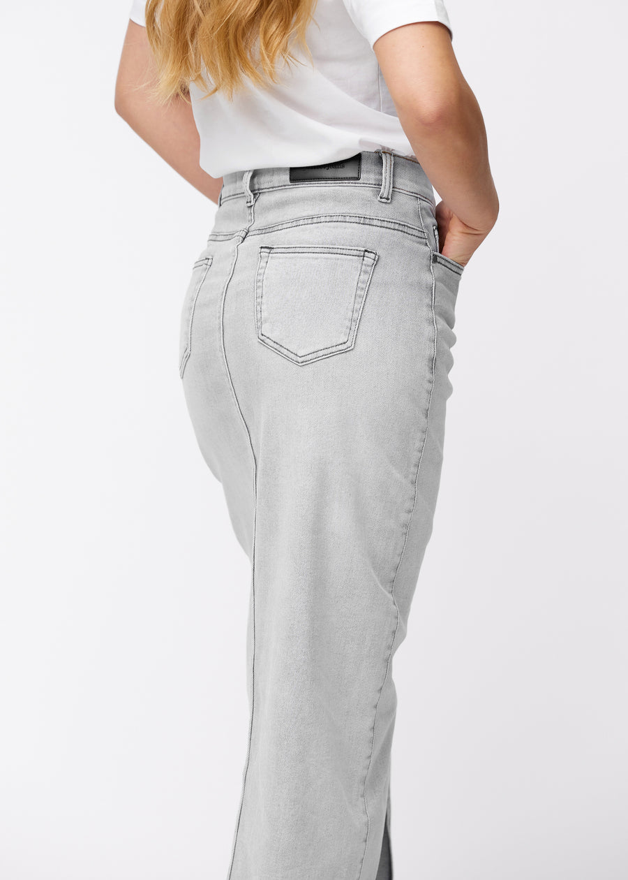 Langer hellgrauer Denimrock für Damen in der Farbe Ashes. Nahaufnahme der Rückseite an einem Model, um Passform und Details zu zeigen.