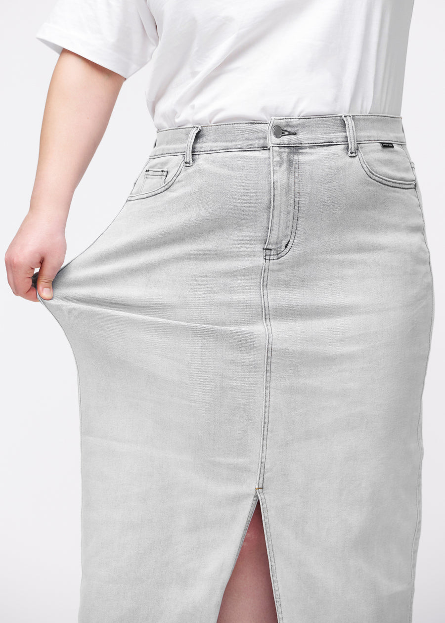 Langer hellgrauer Denimrock für Damen in der Farbe Ashes. Ein Plus-Size-Model dehnt den Stoff an der Hüfte, um den Stretch zu zeigen.