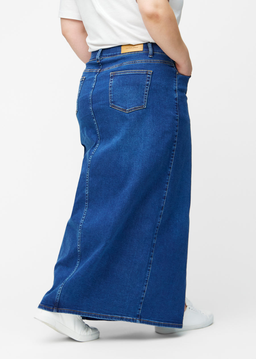 Lang, mørkeblå denimnederdel i farven Oceans med regulær pasform set bagfra på plus-size model, så hele nederdelens længde kan ses.