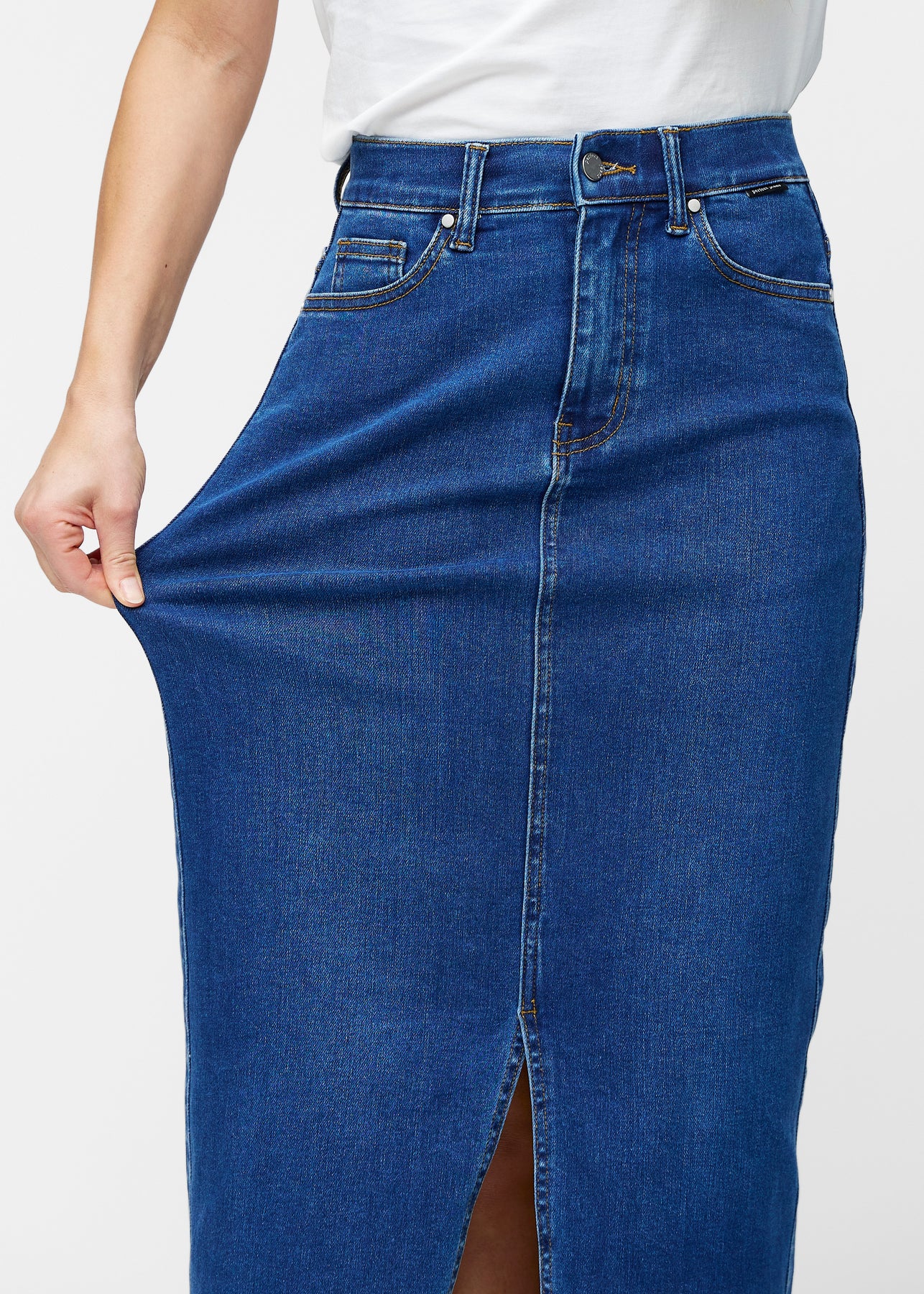Model strækker den lange, mørkeblå denimnederdel i farven Oceans ved hoften for at vise materialets stretch.