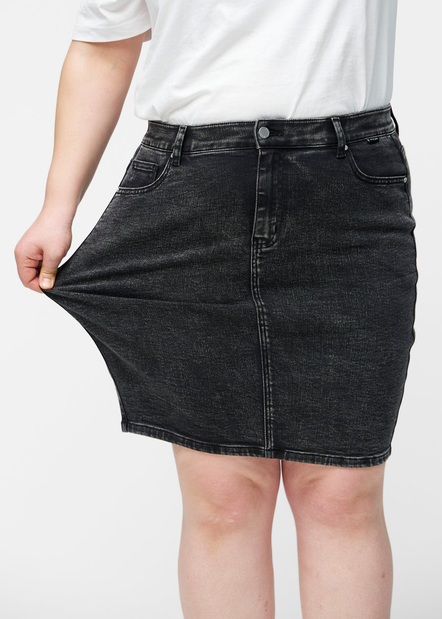 Plus-size model strækker mørkegrå, tætsiddende og knælang denimnederdel ved låret for at vise stretch.