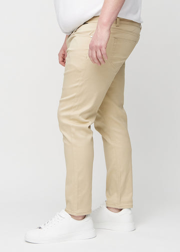 Beigefarbene Jeans im Slim Fit, von der Seite an einem Plus-Size-Model gesehen.