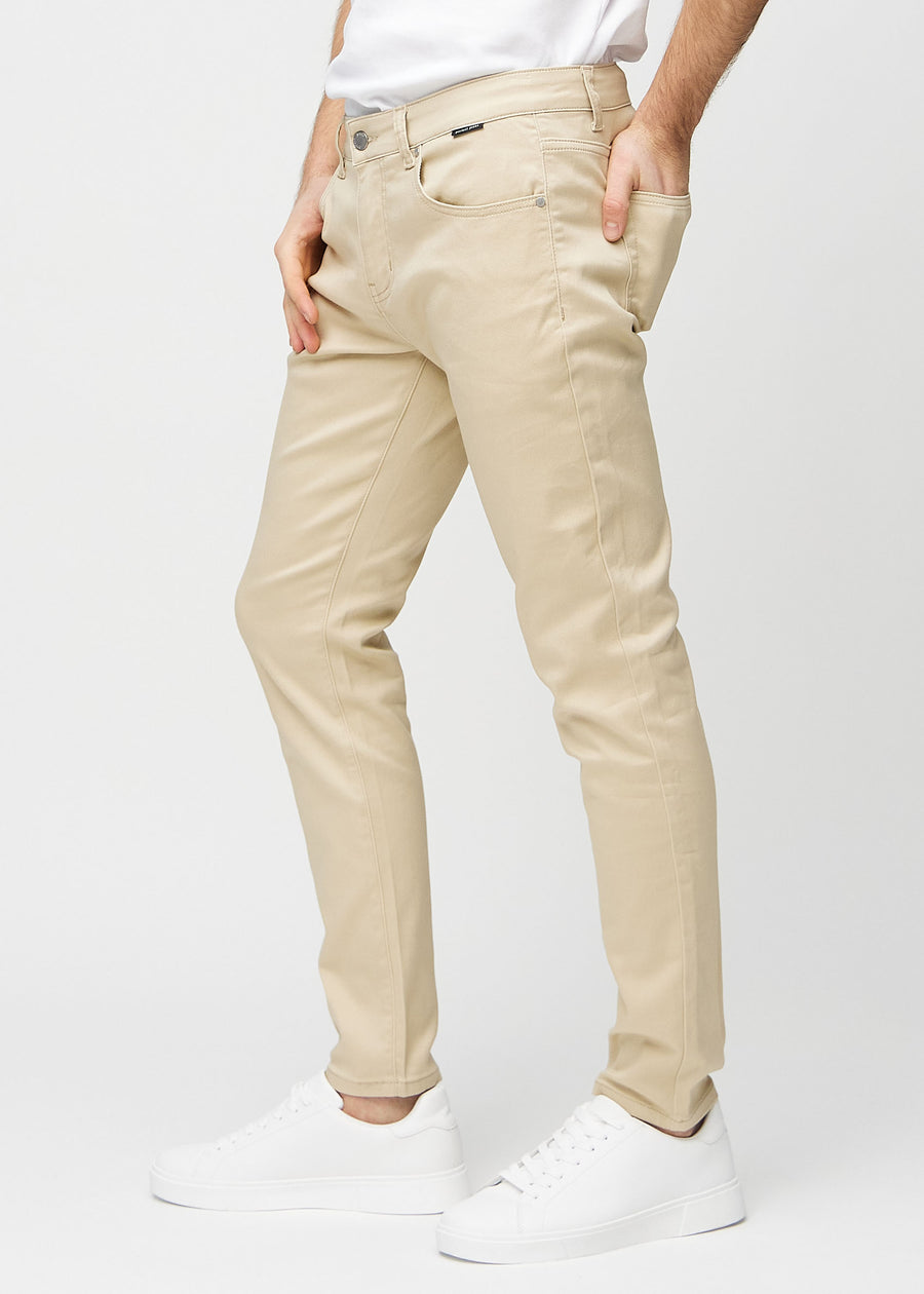 Beigefarbene Jeans im Slim Fit, von der Seite an einem Model gesehen.