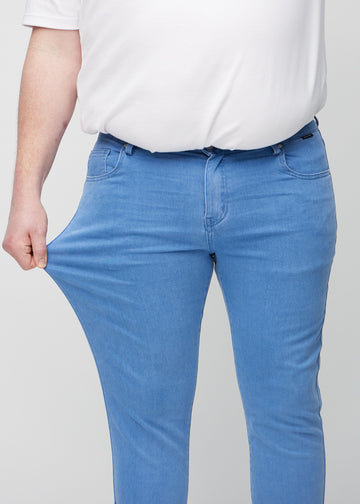 Ein Plus-Size-Model dehnt die Jeans am Oberschenkel, um den Stretch des Materials zu zeigen.