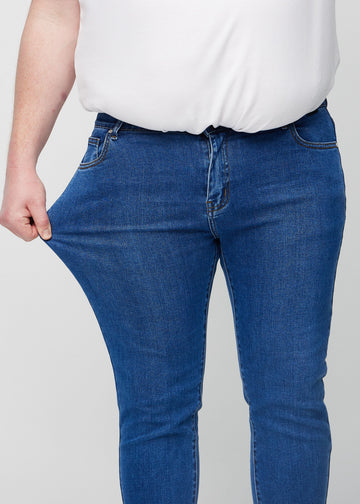 Ein Plus-Size-Model dehnt die Jeans am Oberschenkel, um den Stretch des Materials zu zeigen.