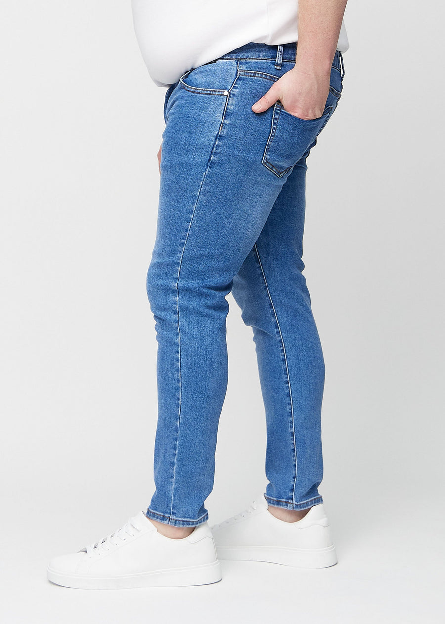 Blaue Denim-Jeans im Slim Fit, von der Seite an einem Plus-Size-Model gesehen.