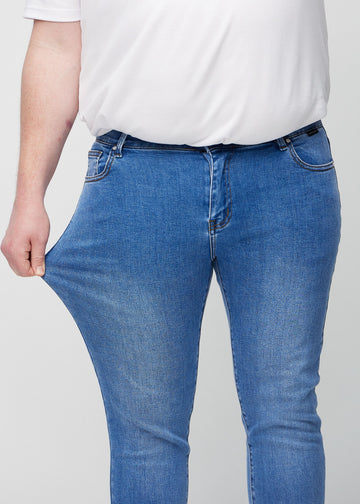 Ein Plus-Size-Model dehnt die Jeans am Oberschenkel, um den Stretch des Materials zu zeigen.