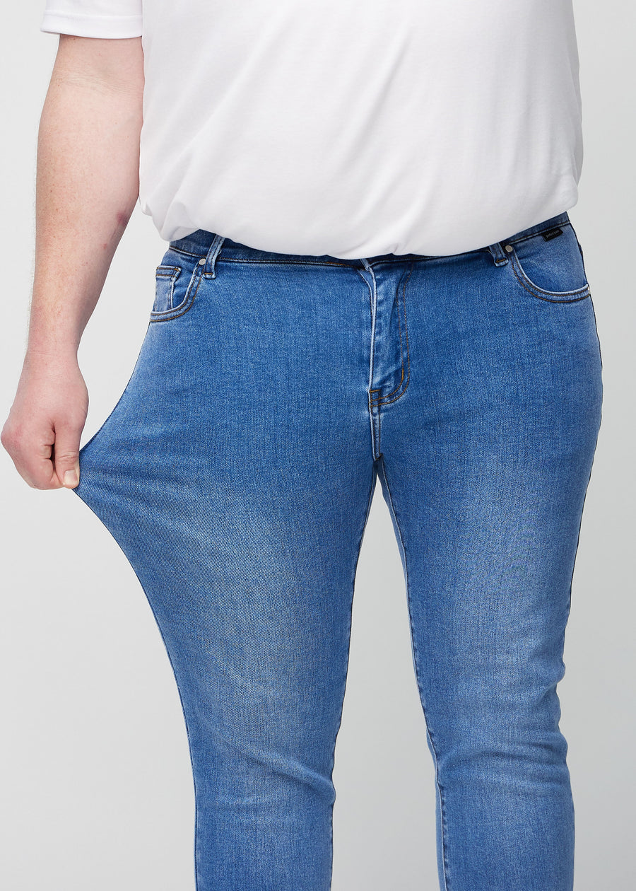 Ein Plus-Size-Model dehnt die Jeans am Oberschenkel, um den Stretch des Materials zu zeigen.