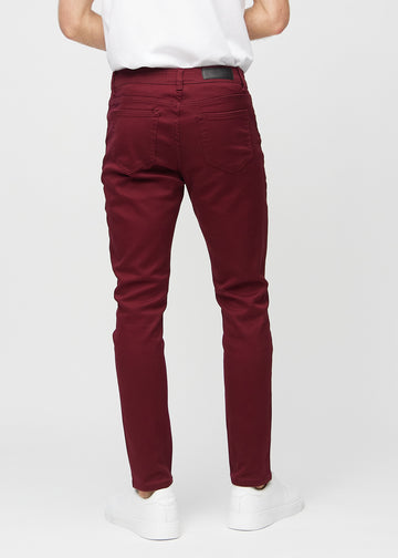 Dunkelrote Jeans im Slim Fit, von hinten gesehen, um die gesamte Jeans zu zeigen.