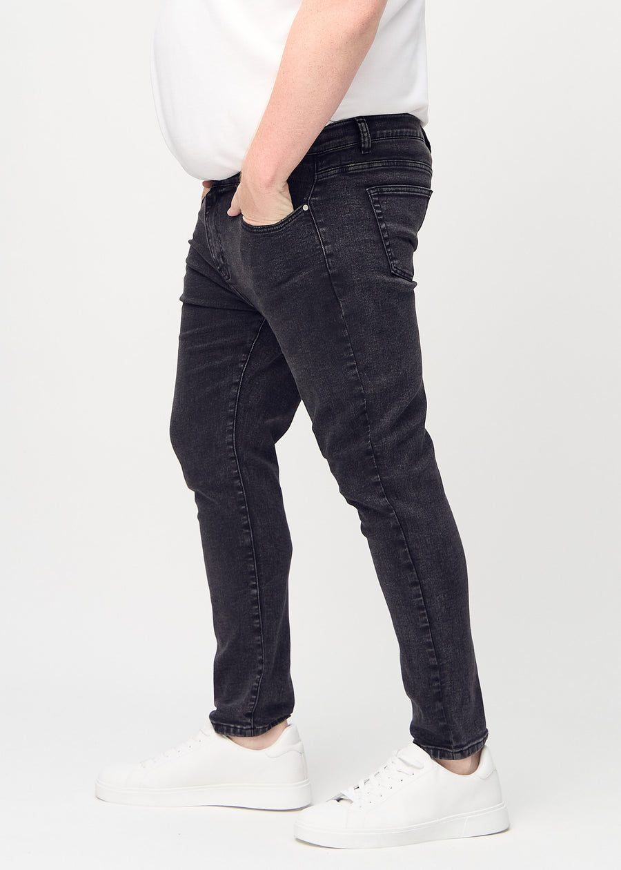 Dunkelgraue Denim-Jeans im Slim Fit, von der Seite an einem Plus-Size-Model gesehen.