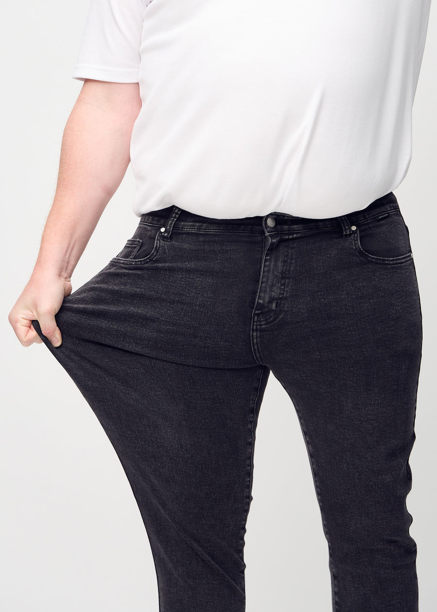 Ein Plus-Size-Model dehnt die Jeans am Oberschenkel, um den Stretch des Materials zu zeigen.