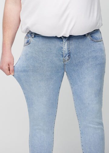 Ein Plus-Size-Model dehnt die Jeans am Oberschenkel, um den Stretch des Materials zu zeigen.